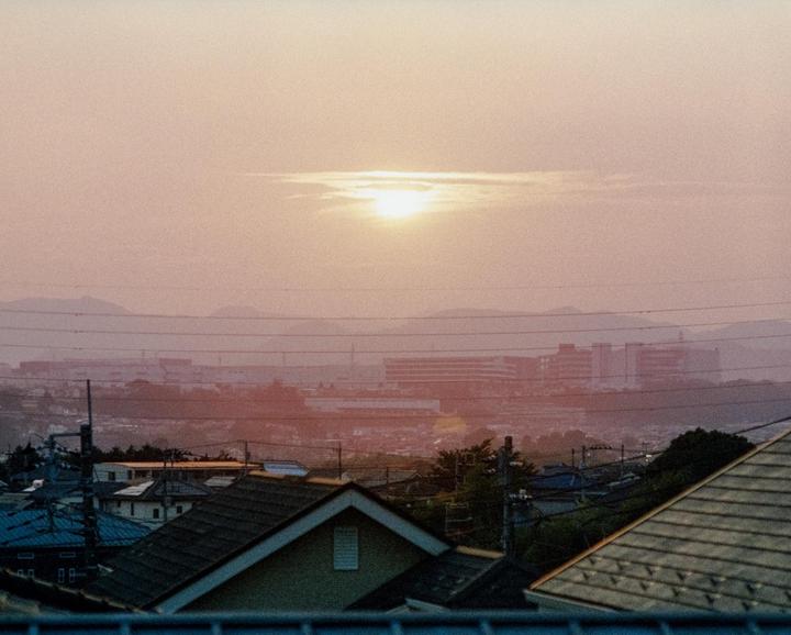 The sun sets over a town with mountains in the distance and power lines crisscrossing the sky.