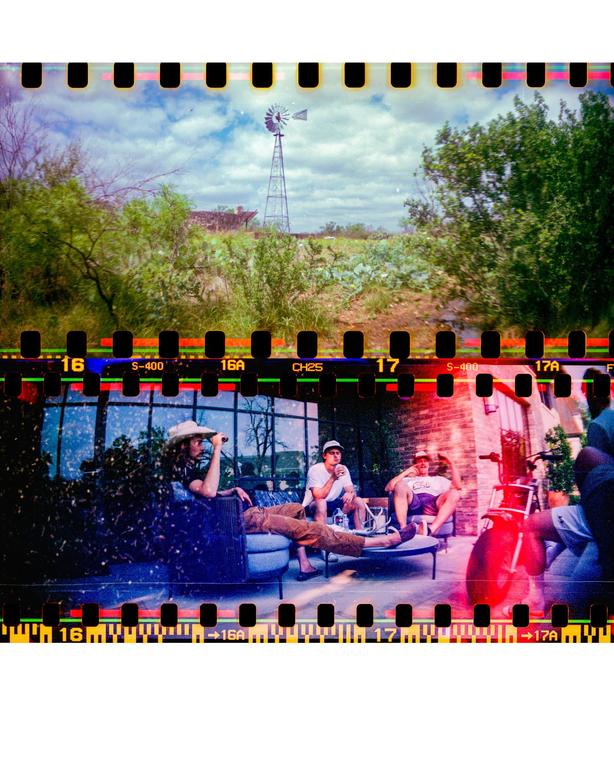 A double exposure shows a windmill in a field above three men relaxing on a patio.