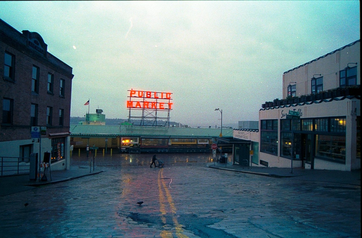 A person pushes a cart on a wet street in front of the Public Market sign.