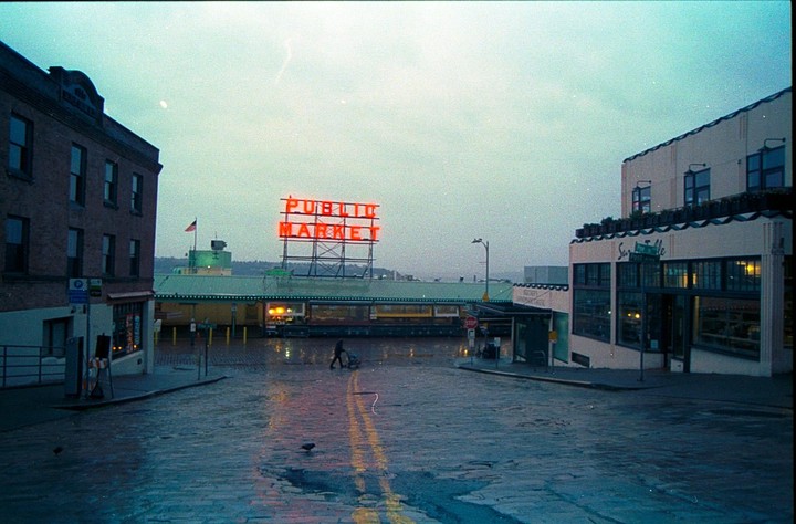 A person pushes a cart on a wet street in front of the Public Market sign.
