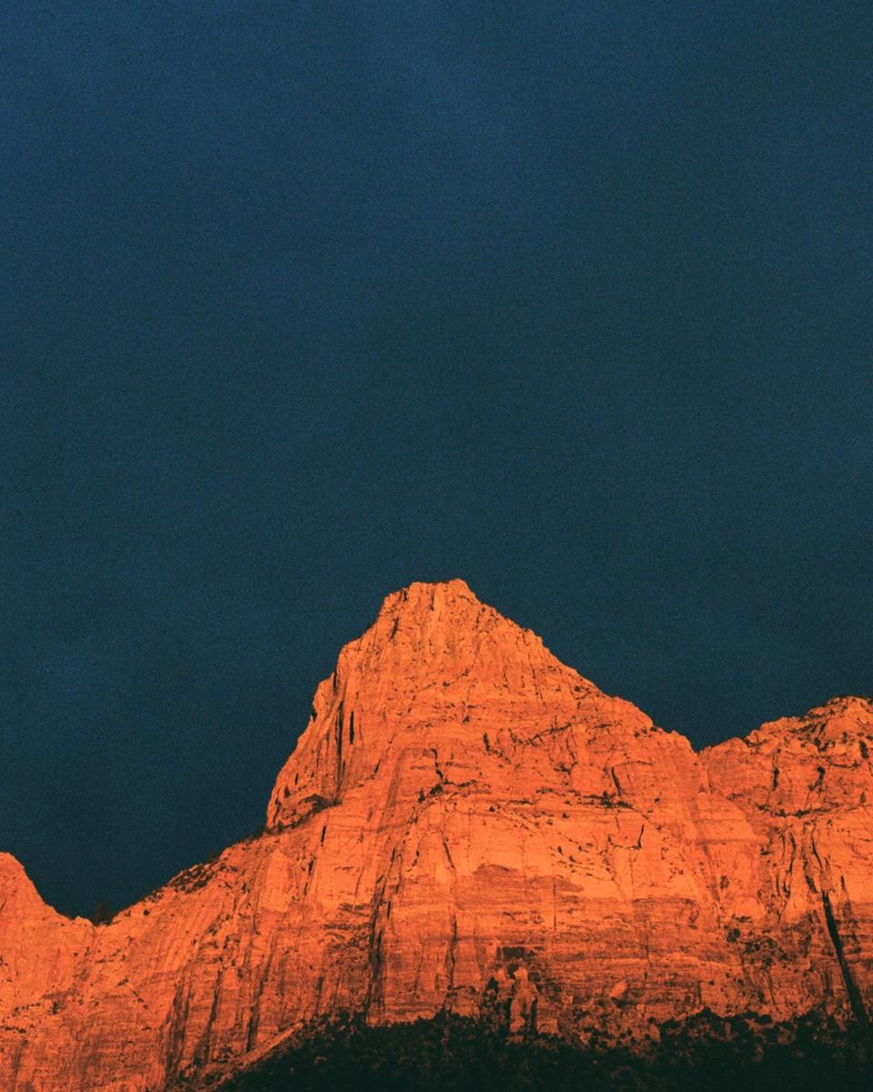 A mountain peak is illuminated by golden light against a dark blue sky.