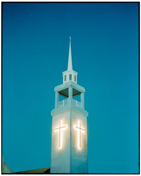 A church steeple with two illuminated crosses is visible against a dark blue sky.