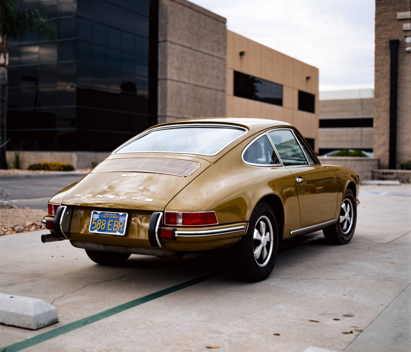A gold Porsche is parked on a concrete surface in front of a modern building.