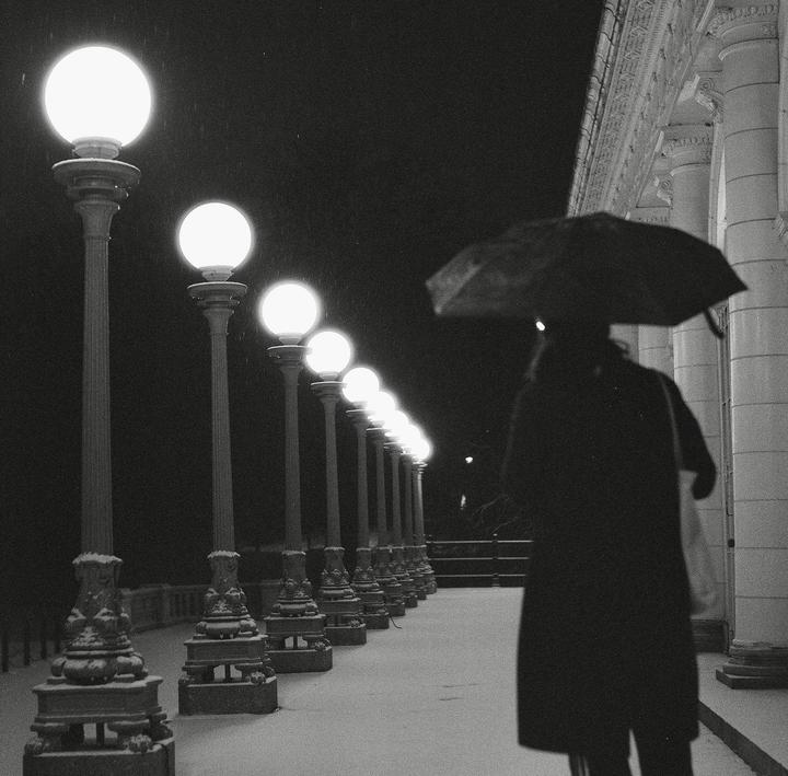 A person with an umbrella walks past a row of glowing streetlights on a snowy night.