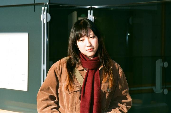 A woman with long hair and a red scarf stands in front of a glass door.