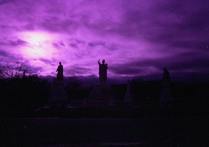 Three statues are silhouetted against a vibrant purple sky with clouds and faint stars.