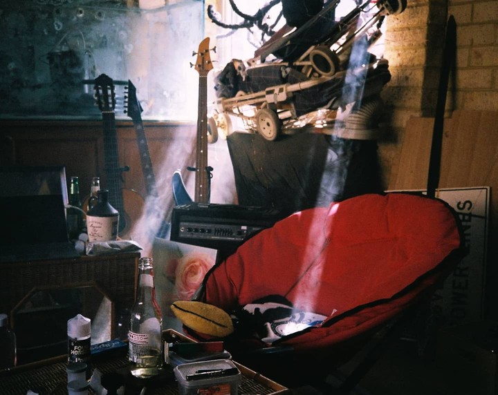 Sunlight streams into a cluttered garage, illuminating a red chair, musical instruments, and various objects.