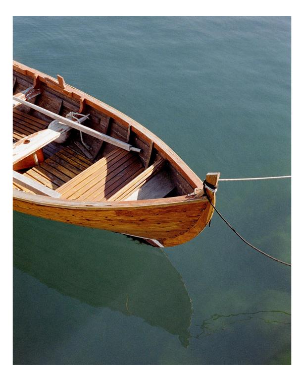 A wooden rowboat is moored in calm water, casting a reflection.