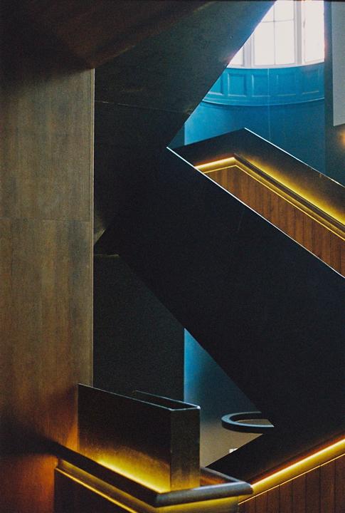 A modern staircase with illuminated handrails leads up towards a window and a blue wall.