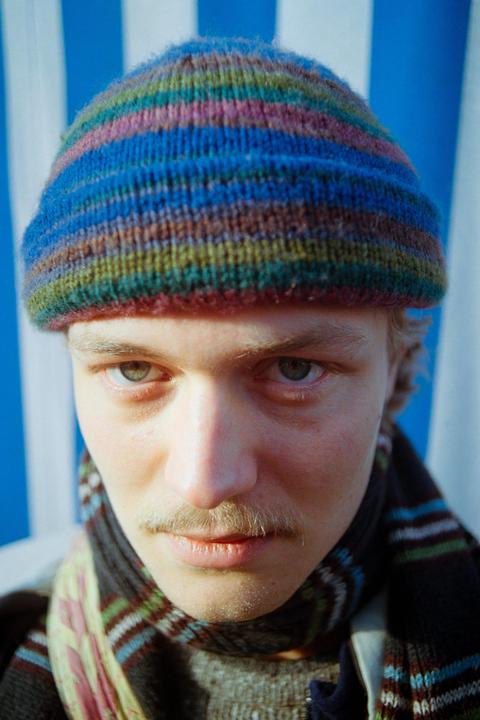 A man with a mustache and a colorful striped beanie looks directly at the viewer.