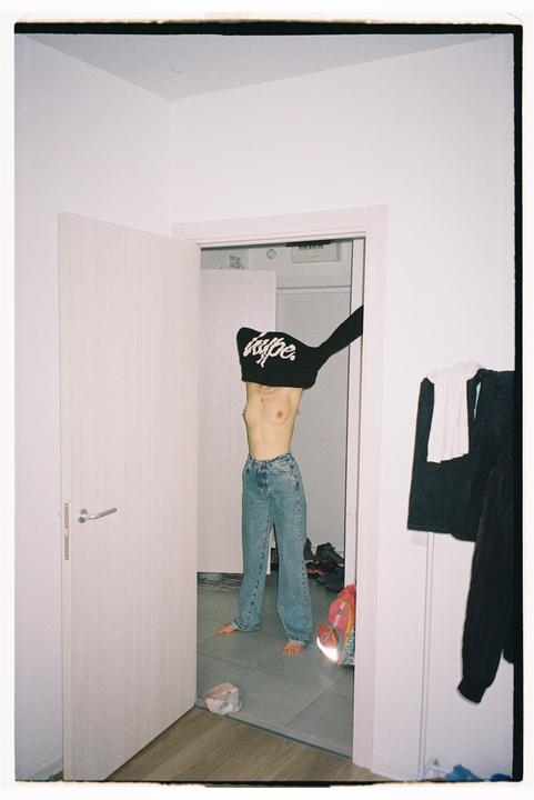 A woman stands in a doorway, pulling a black sweatshirt over her head.