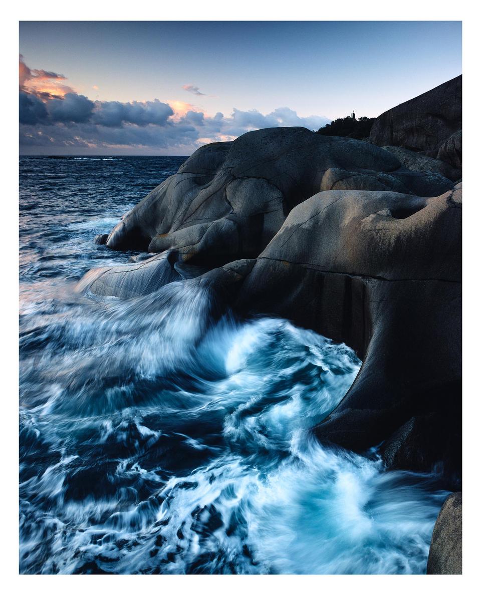 Waves crash against a rocky coastline under a dramatic sky at dusk.