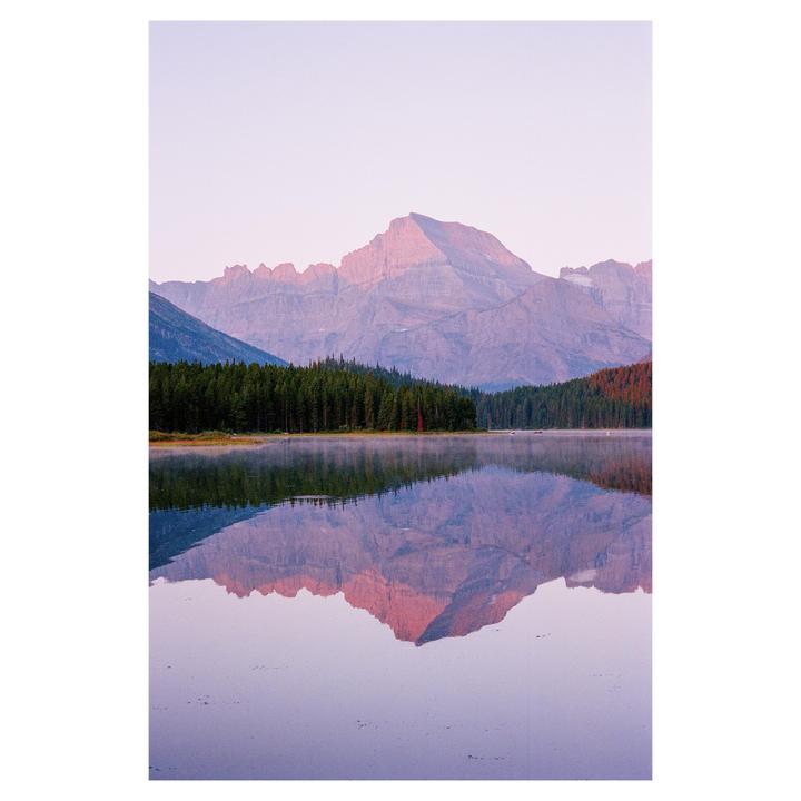 A mountain range with a forest at its base is reflected in a still lake.