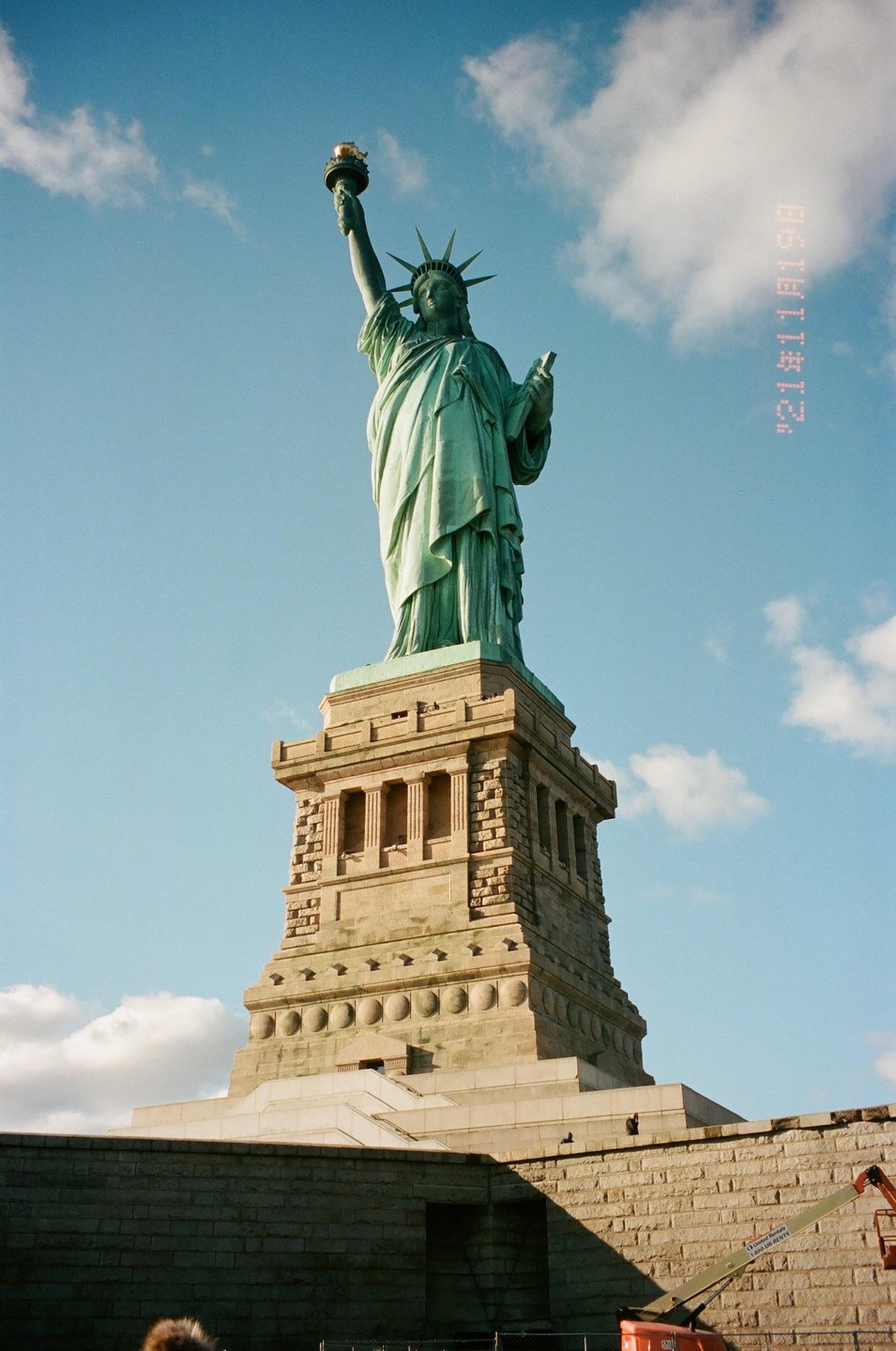 The Statue of Liberty stands tall against a blue sky with scattered clouds.