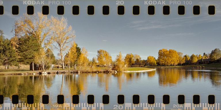A body of water reflects trees with autumn foliage under a clear sky.