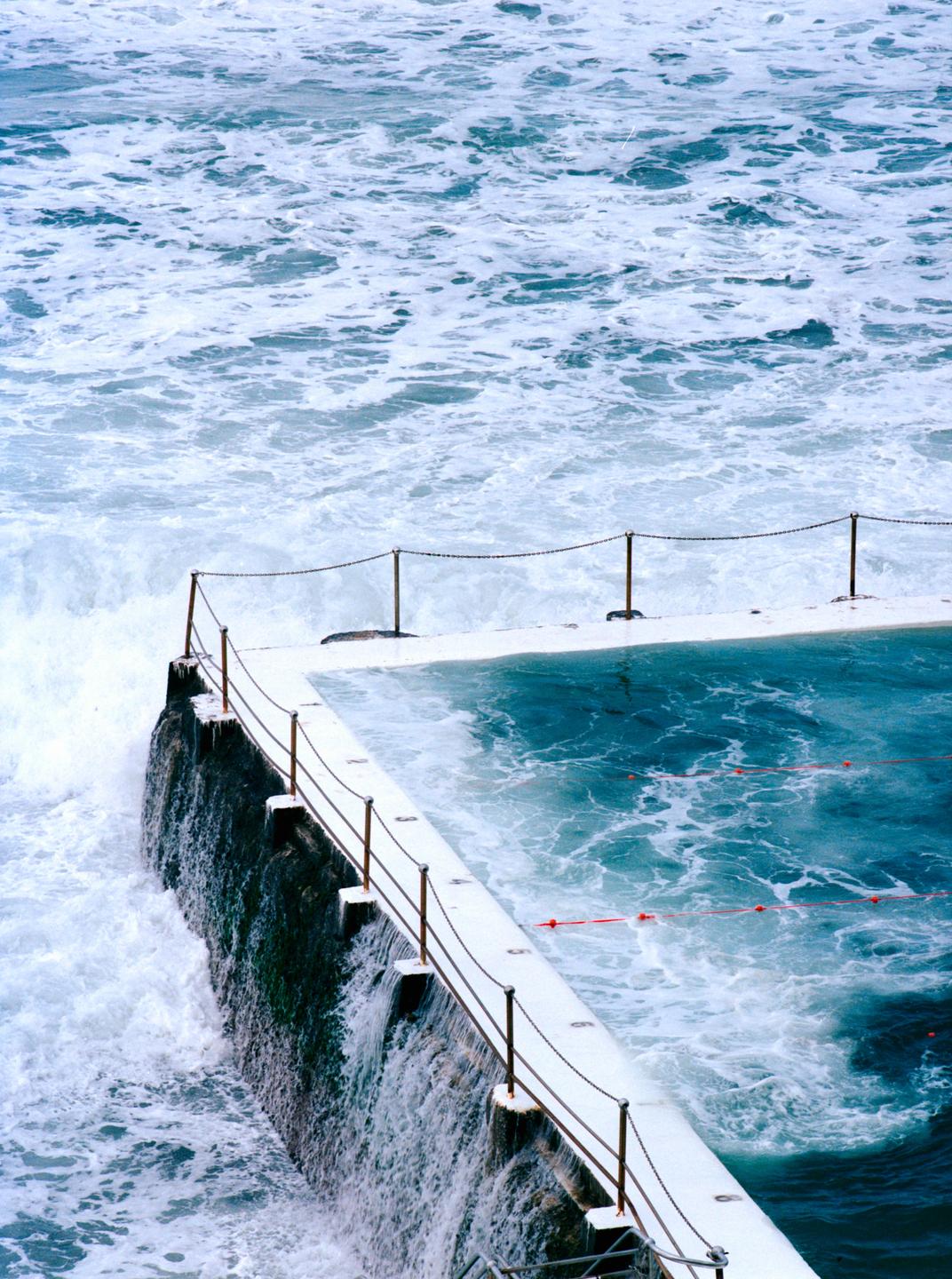 Waves crash over the edge of a swimming pool built into the ocean.