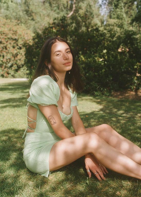 A woman in a green dress sits on the grass with dappled sunlight on her body.