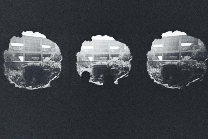 Three circular windows look out onto a building with balconies and lush foliage.