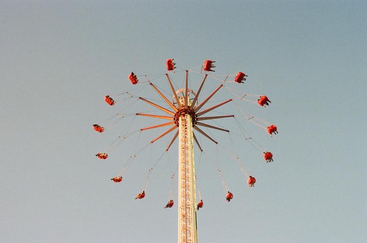 A swing ride with people in red seats is captured against a clear sky.