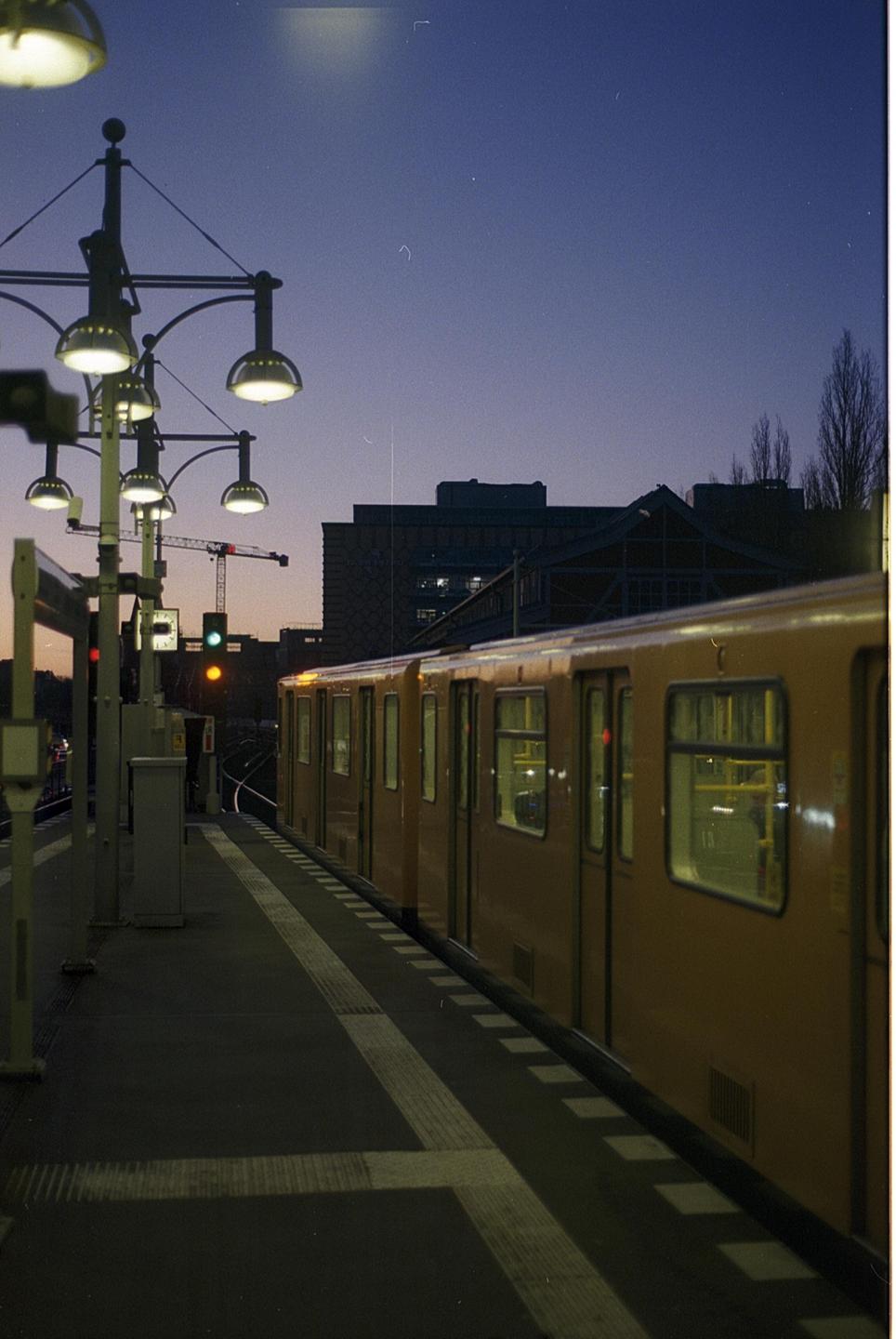 A yellow train is stopped at a station platform at dusk, with streetlights illuminating the scene.