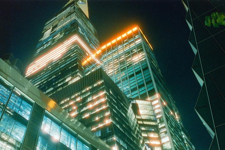 Multiple skyscrapers with illuminated windows are visible from a low angle at night.