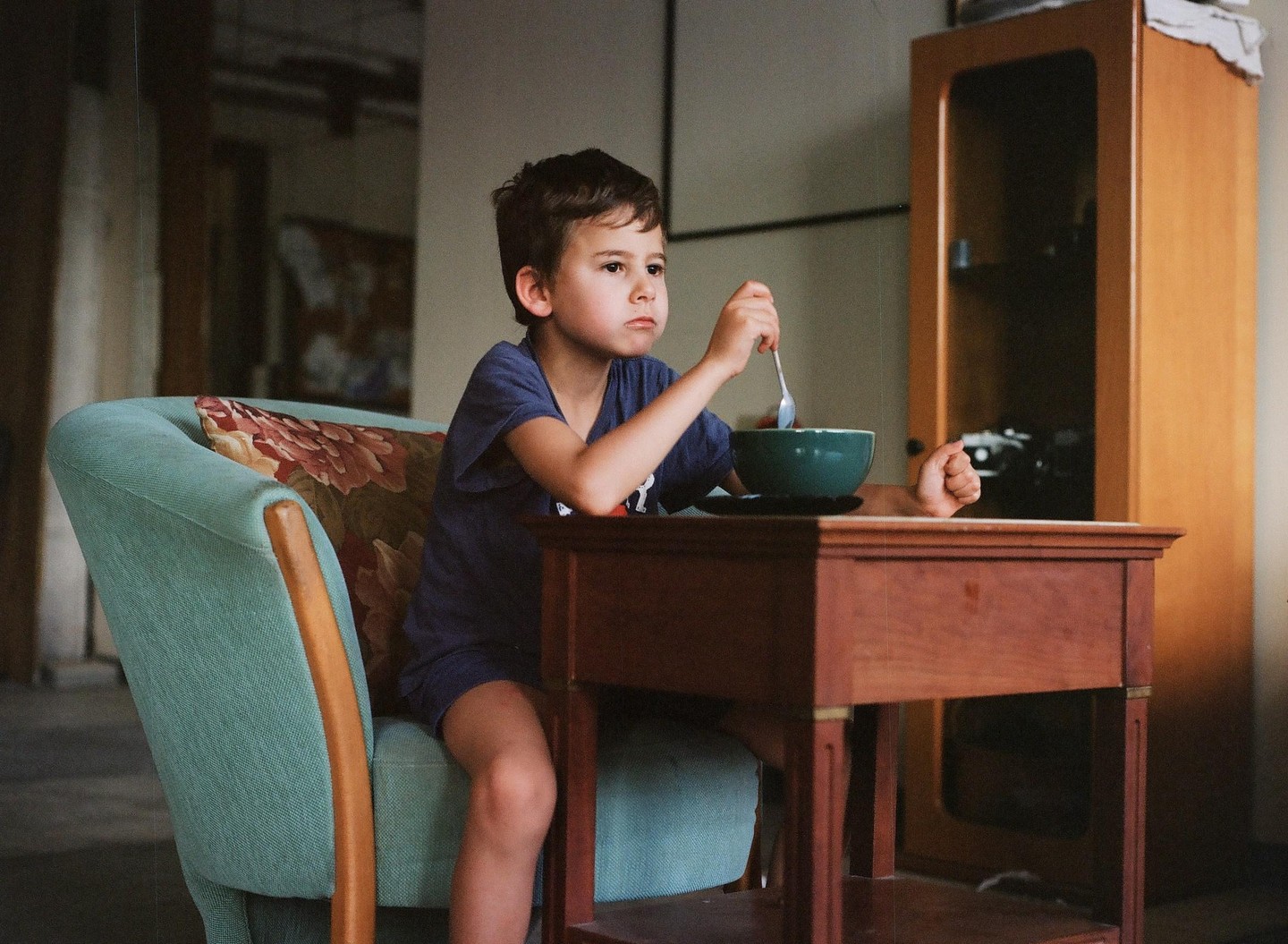 A boy sits in a chair at a table with a bowl and spoon.