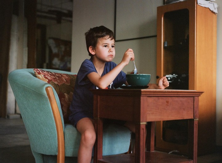 A boy sits in a chair at a table with a bowl and spoon.