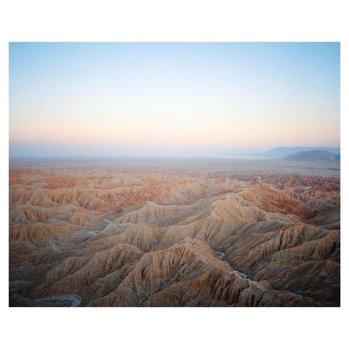 A vast desert landscape with intricate badlands stretches under a pastel sky at dusk.