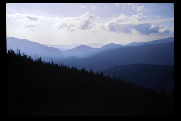 A mountain range with a dark forested slope in the foreground is visible under a cloudy sky.