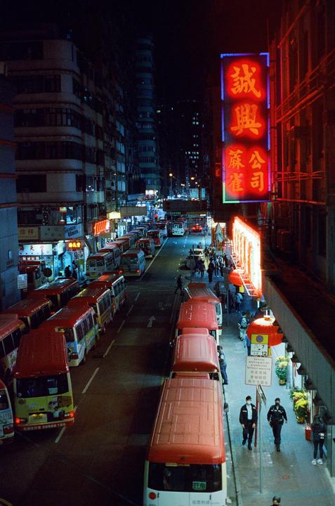 A street in Hong Kong is filled with buses and people at night, illuminated by neon signs.