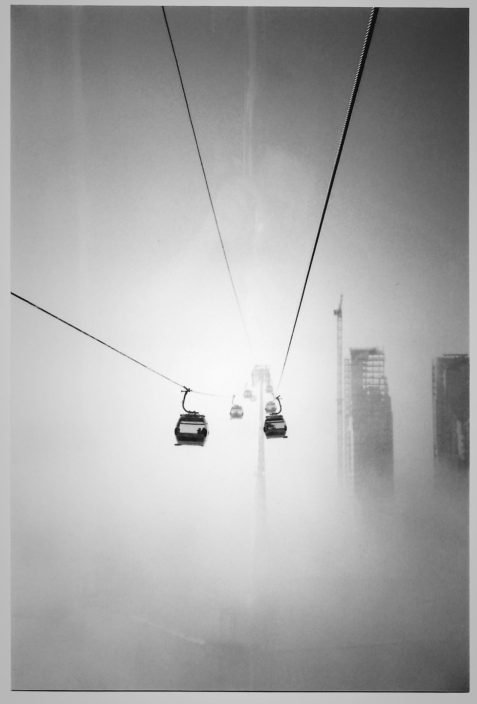 Several cable car gondolas are visible on a foggy day with tall buildings in the background.