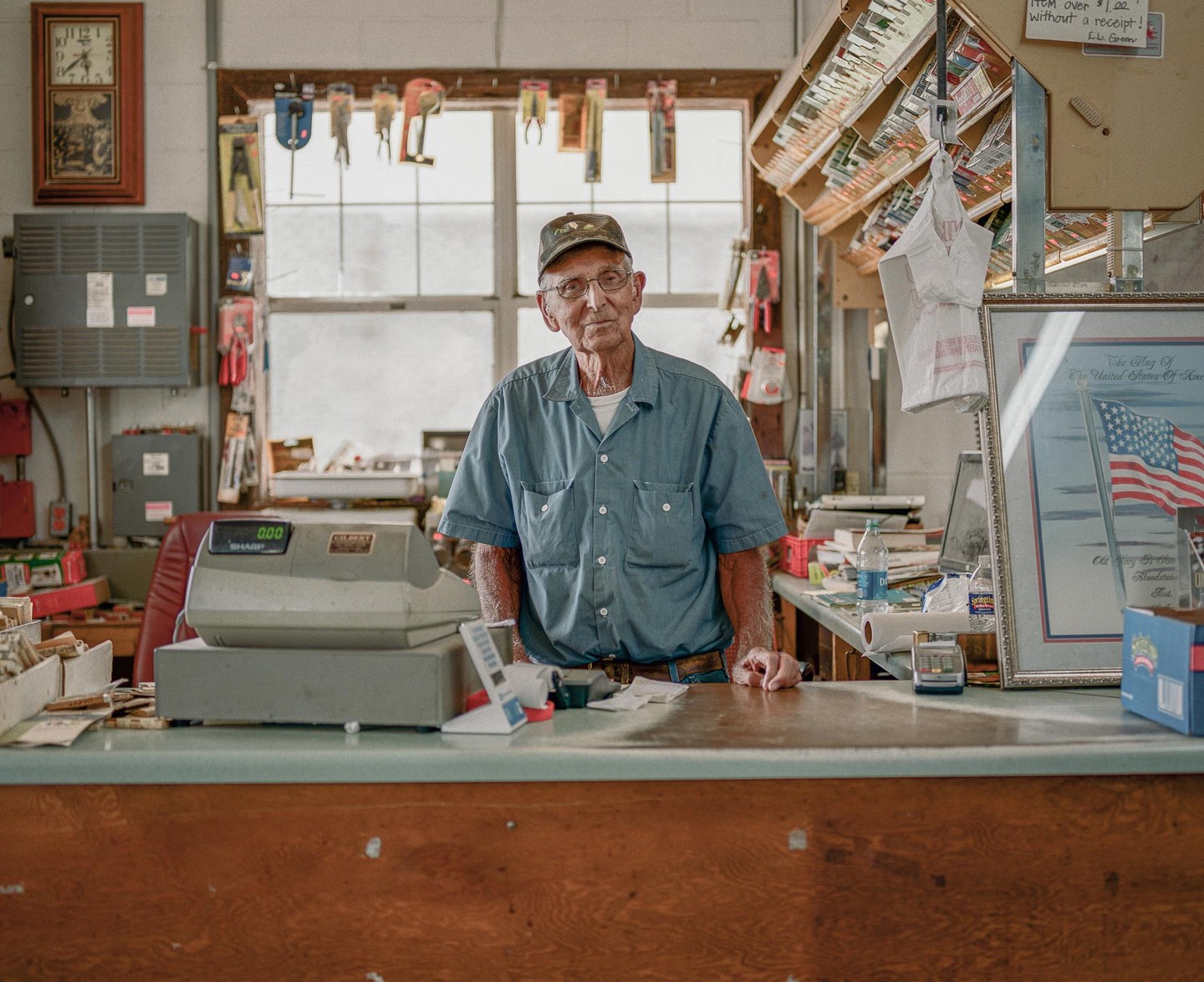 An elderly man stands behind a counter in a general store.