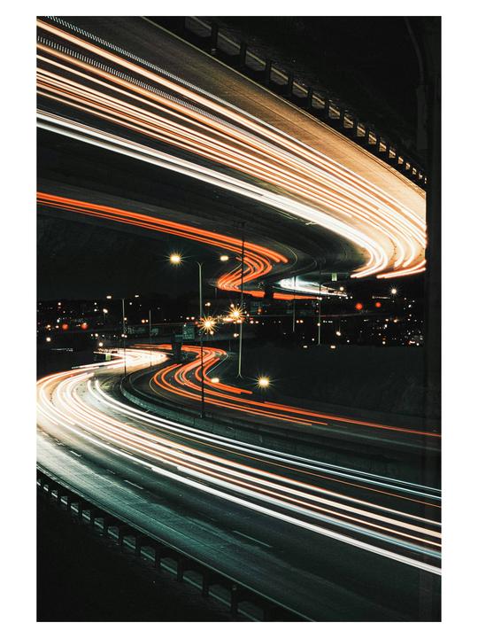 Light trails from vehicles on a multi-level highway interchange are visible at night.
