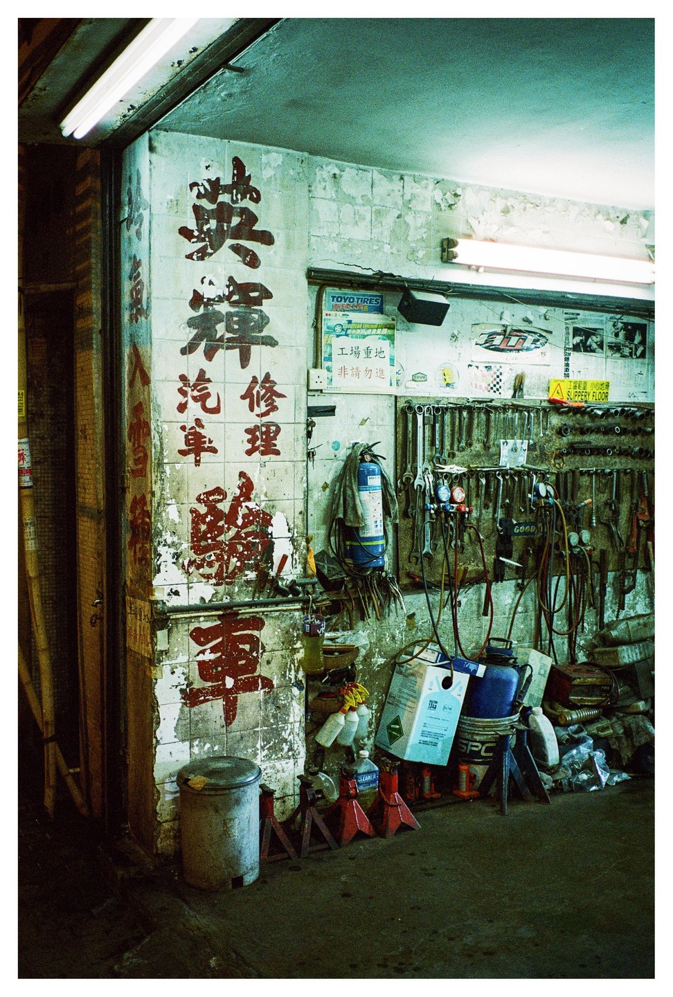 A cluttered garage interior shows tools hanging on a wall, a fire extinguisher, and various containers on the floor.