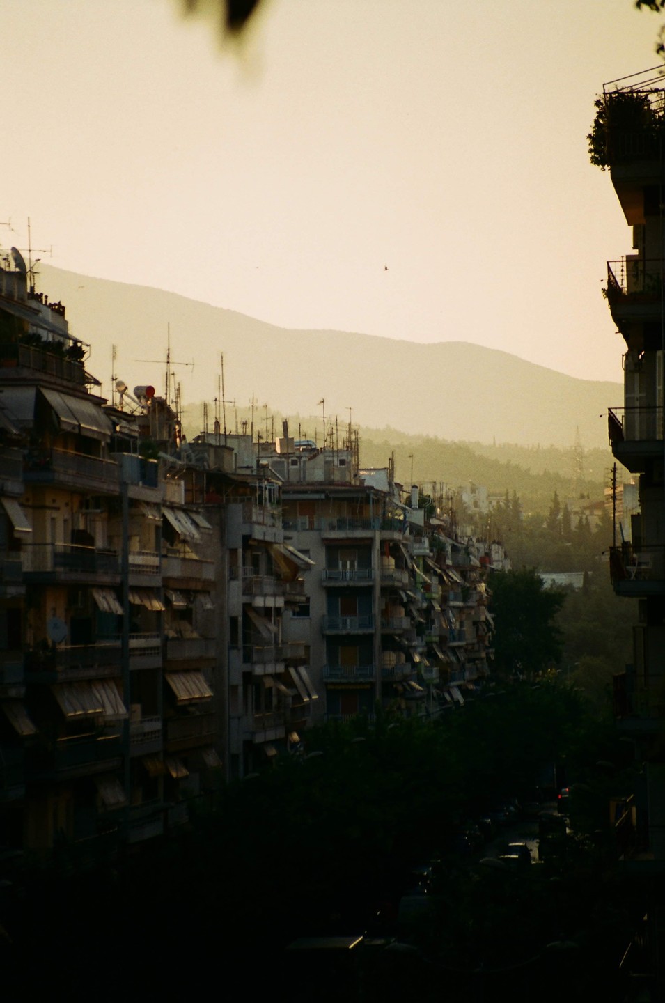 A row of apartment buildings with awnings and antennas on their roofs is visible under a hazy sky with mountains in the background.
