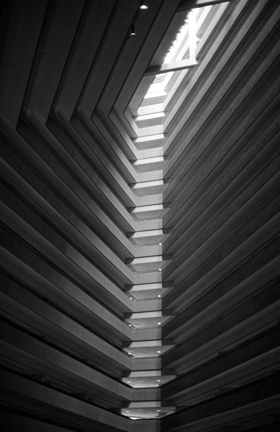 A low angle view shows the interior of a tall building with many floors and a skylight at the top.