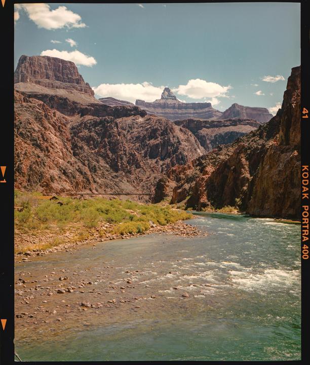 A river flows through a canyon with steep, rocky walls under a partly cloudy sky.