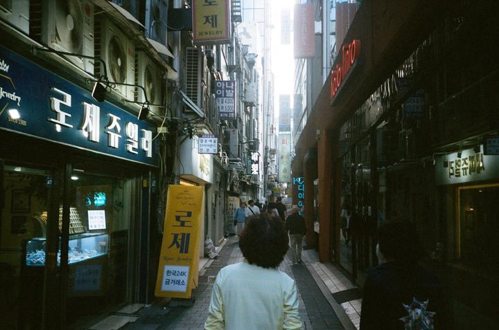 A person walks down a narrow street lined with buildings and signs.