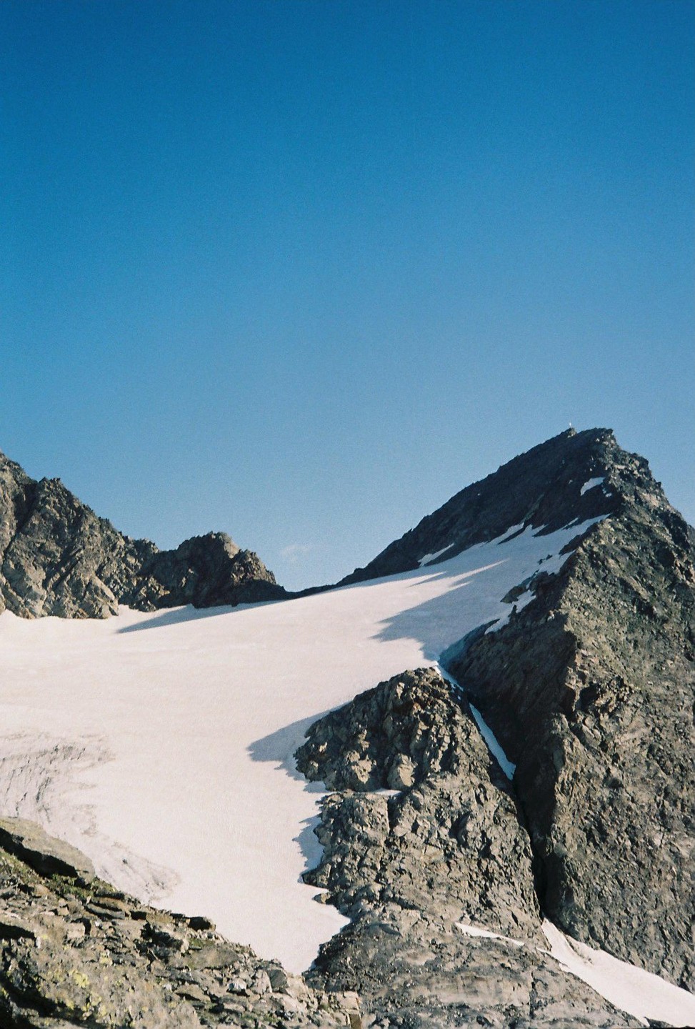 A snow-covered mountain peak with rocky slopes is visible under a clear blue sky.