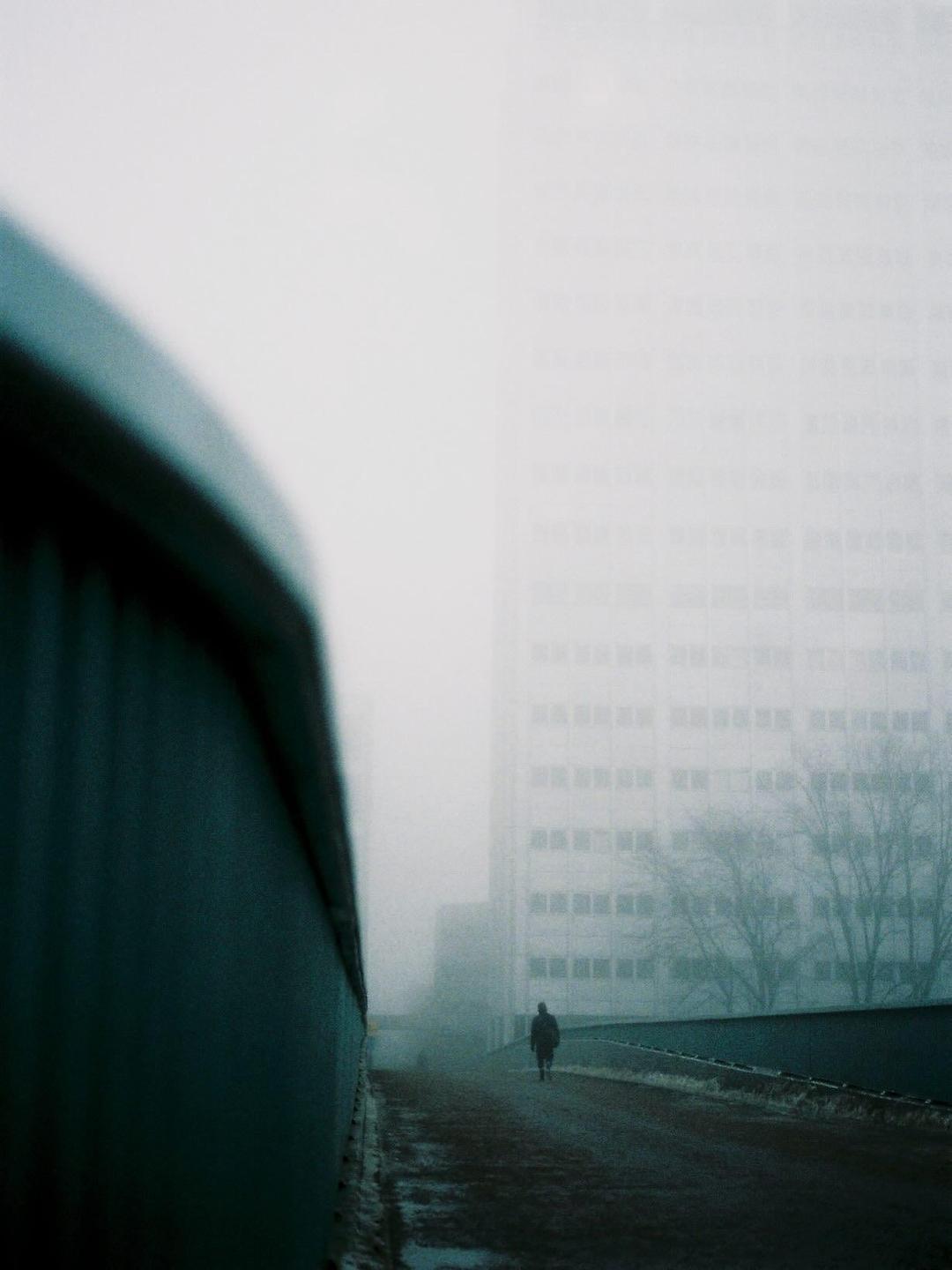 A person walks on a foggy street next to a tall building.