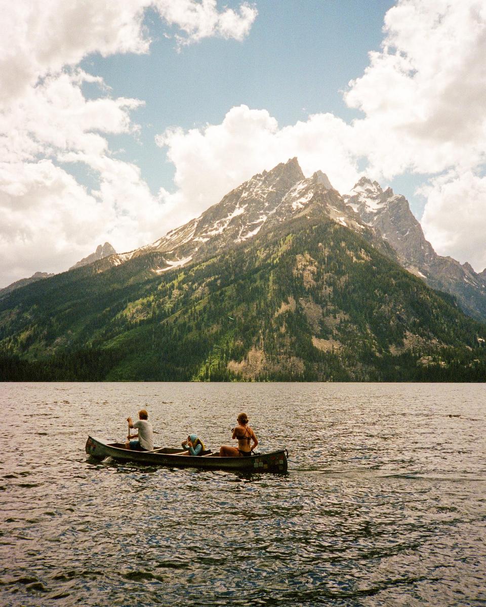 A man, woman, and child are in a canoe on a lake with a large mountain in the background.
