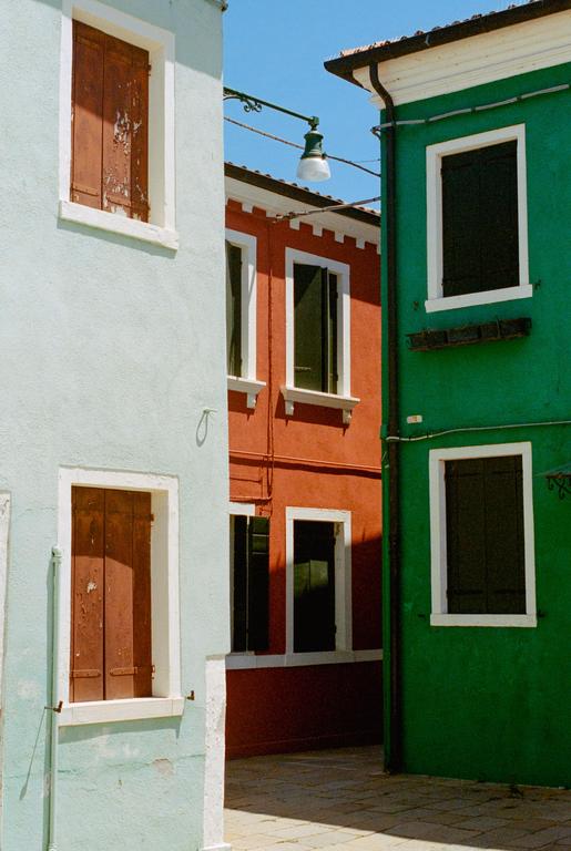 Three brightly colored buildings with windows and shutters are visible under a clear sky.