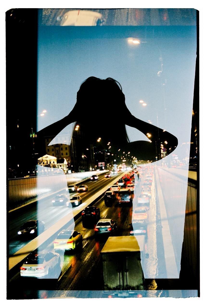 A double exposure shows the silhouette of a woman superimposed over a busy highway at night.