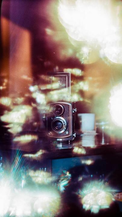 A vintage camera is visible through a window with light reflections.