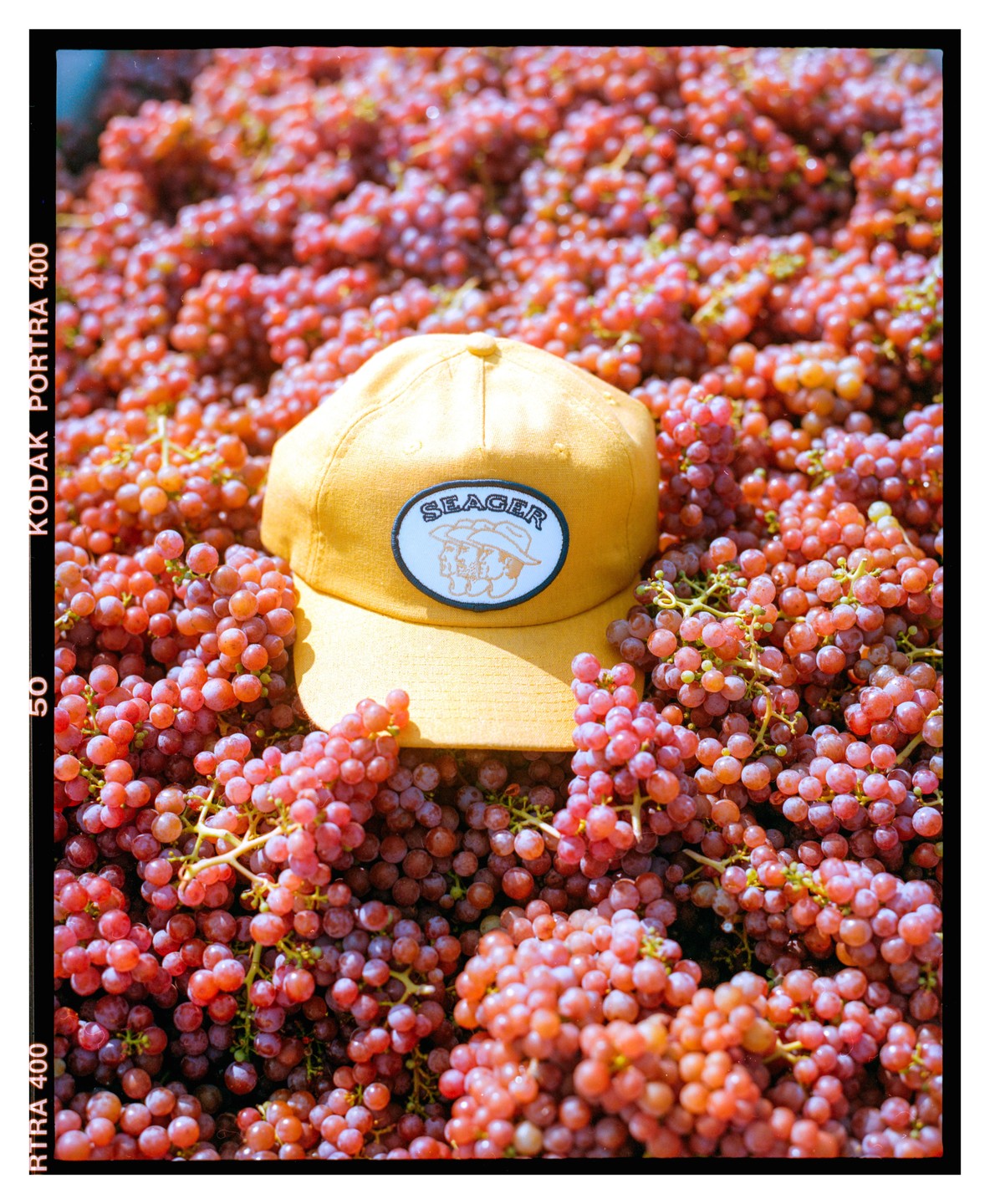 A yellow baseball cap with a "Seager" patch is nestled among a large pile of red grapes.