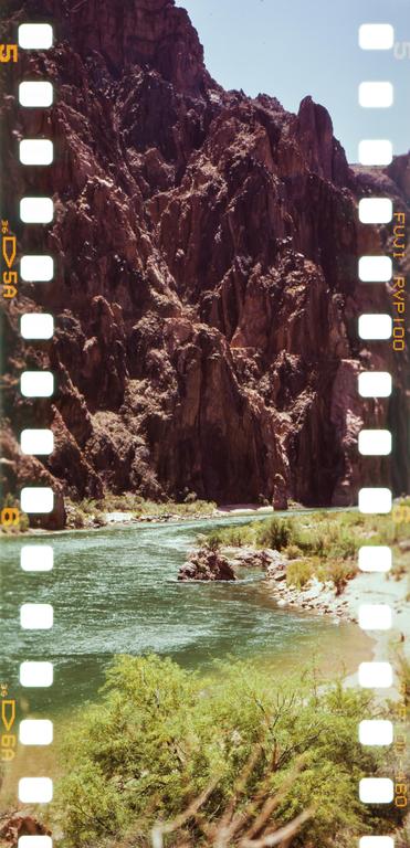 A river flows through a canyon with steep, rocky walls and green foliage on its banks.