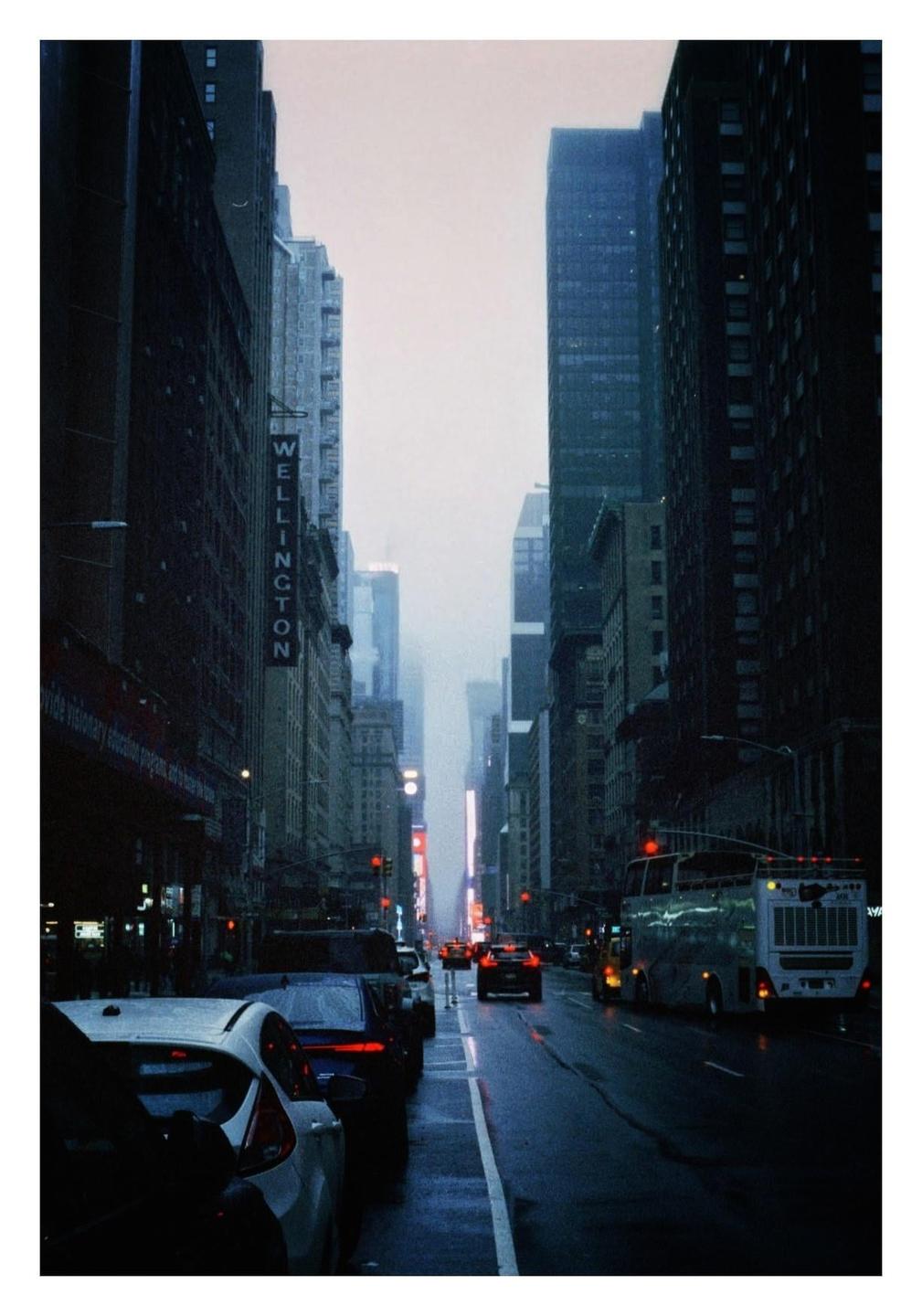 A street in New York City is filled with cars and tall buildings on a rainy day.