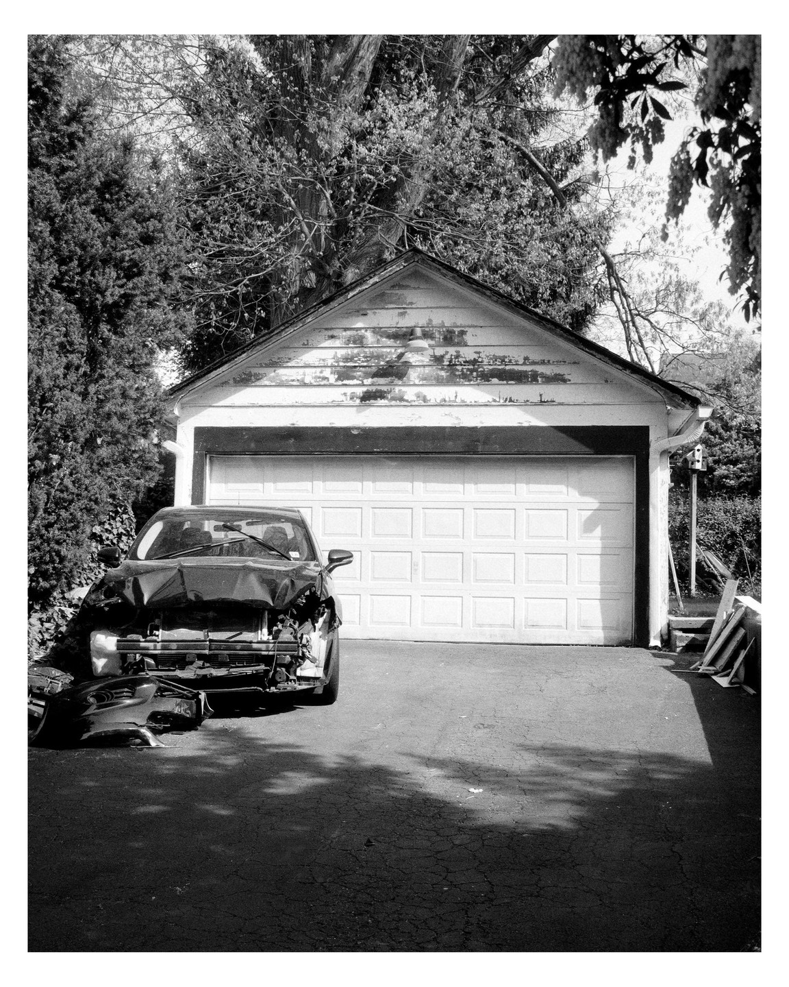 A severely damaged car is parked in a driveway in front of a garage.