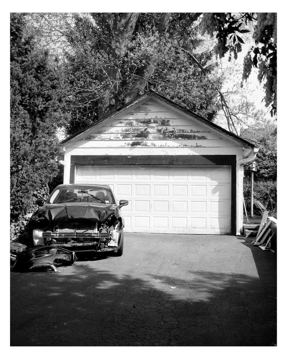 A severely damaged car is parked in a driveway in front of a garage.