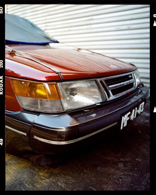 The front of a red car with a blue cover on its windshield is parked in front of a white garage door.